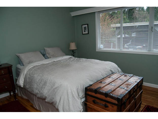 Furnished bedroom with a large bed, wooden floors, and a chest at the foot of the bed. - 5680 Marine Drive, West Vancouver