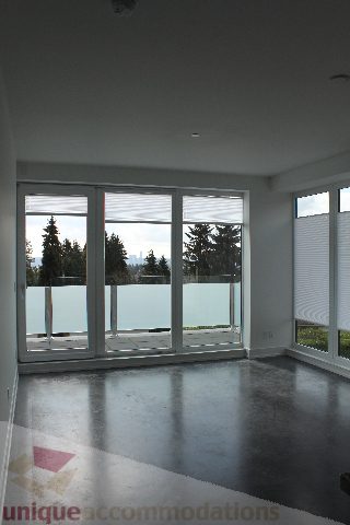 Spacious living room with floor-to-ceiling windows, hardwood floors, and a city view. - 301 - 650 Evergreen Place, North Vancouver
