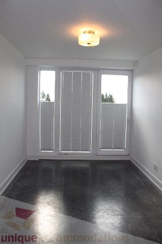 Spacious living room with large windows, black polished concrete floor, and a warm ceiling light. - 301 - 650 Evergreen Place, North Vancouver