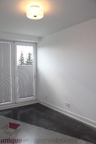 Spacious bedroom with a sliding glass door leading to a balcony, featuring a cozy carpet and a ceiling light.