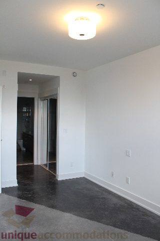 Spacious living room with dark carpet and modern light fixture, perfect for a cozy stay. - 301 - 650 Evergreen Place, North Vancouver