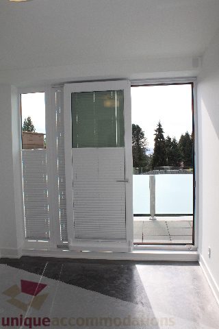 Spacious living room with large sliding glass doors, offering a serene view of the evergreen trees. - 301 - 650 Evergreen Place, North Vancouver
