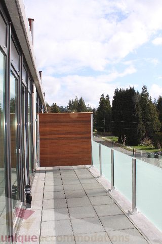 Spacious balcony with wooden privacy screen and glass railings, offering a serene forest view. - 301 - 650 Evergreen Place, North Vancouver