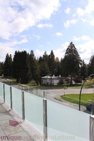 Spacious balcony with glass railings, offering a serene view of evergreen trees and a clear sky. - 301 - 650 Evergreen Place, North Vancouver