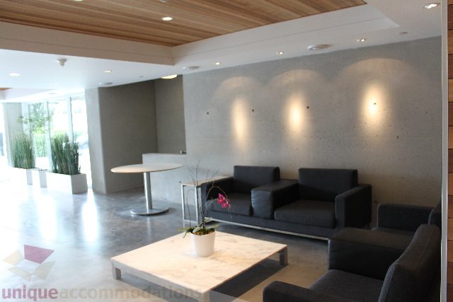 Spacious living room with modern furniture, concrete walls, and natural light from large windows. - 301 - 650 Evergreen Place, North Vancouver