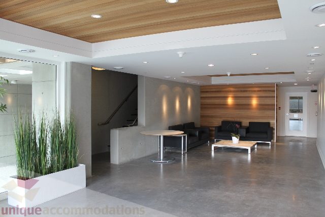 Spacious living room with modern furnishings, wood accents, and large windows. - 301 - 650 Evergreen Place, North Vancouver