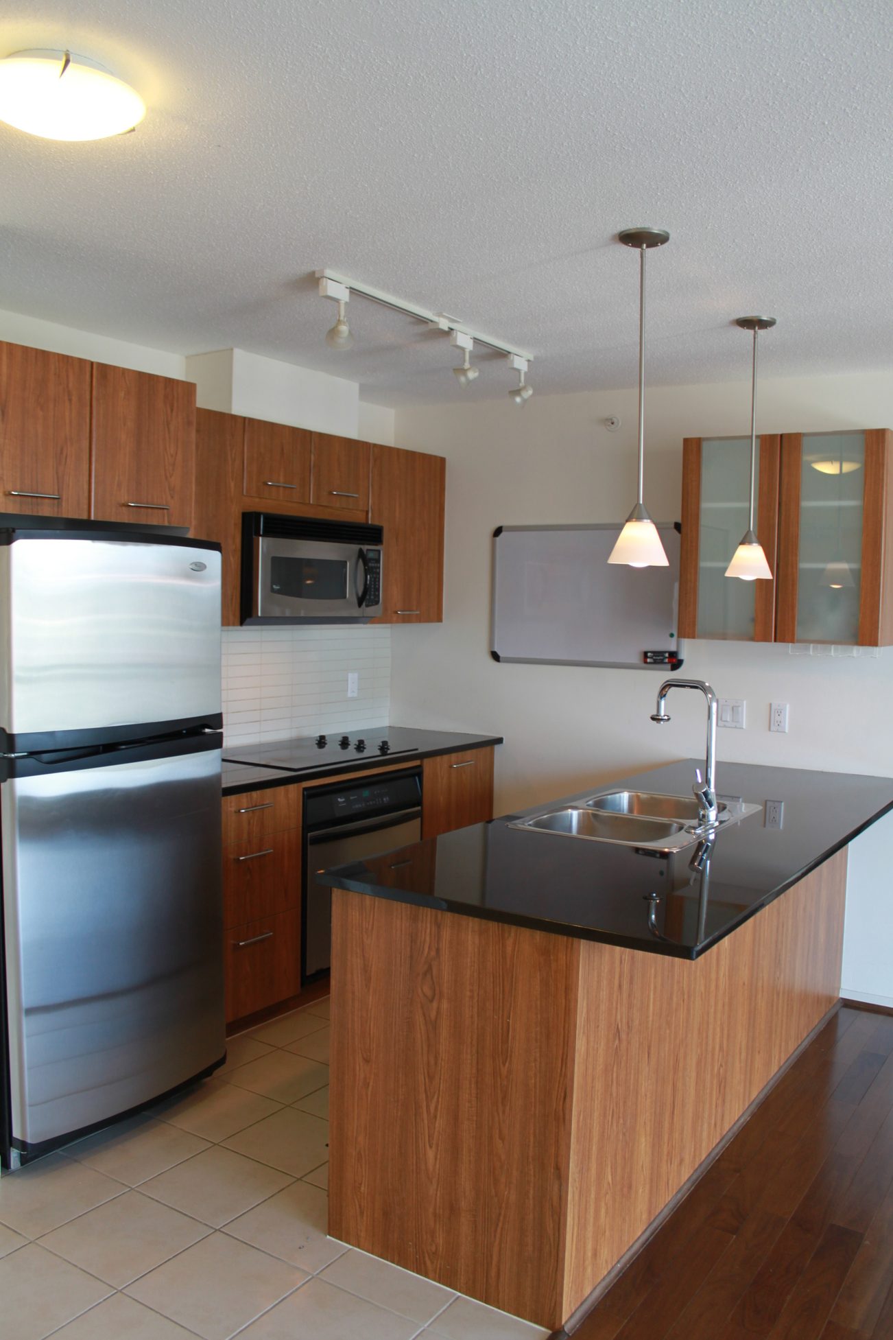 Bright kitchen with dark countertops, stainless steel appliances, and a whiteboard wall. - 2001 - 1199 Seymour, Vancouver Downtown