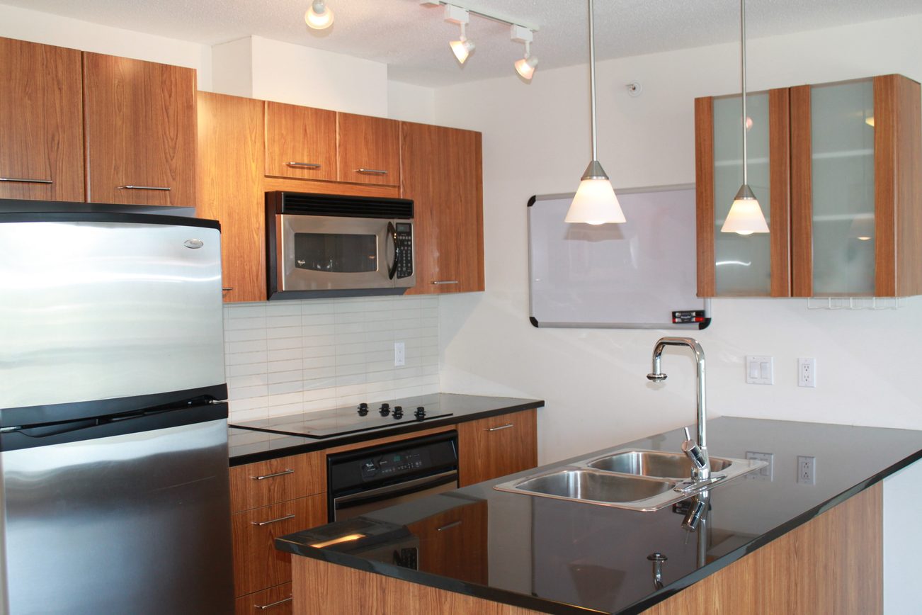 Bright kitchen with modern black countertops, wood cabinets, and stainless steel appliances. - 2001 - 1199 Seymour, Vancouver Downtown