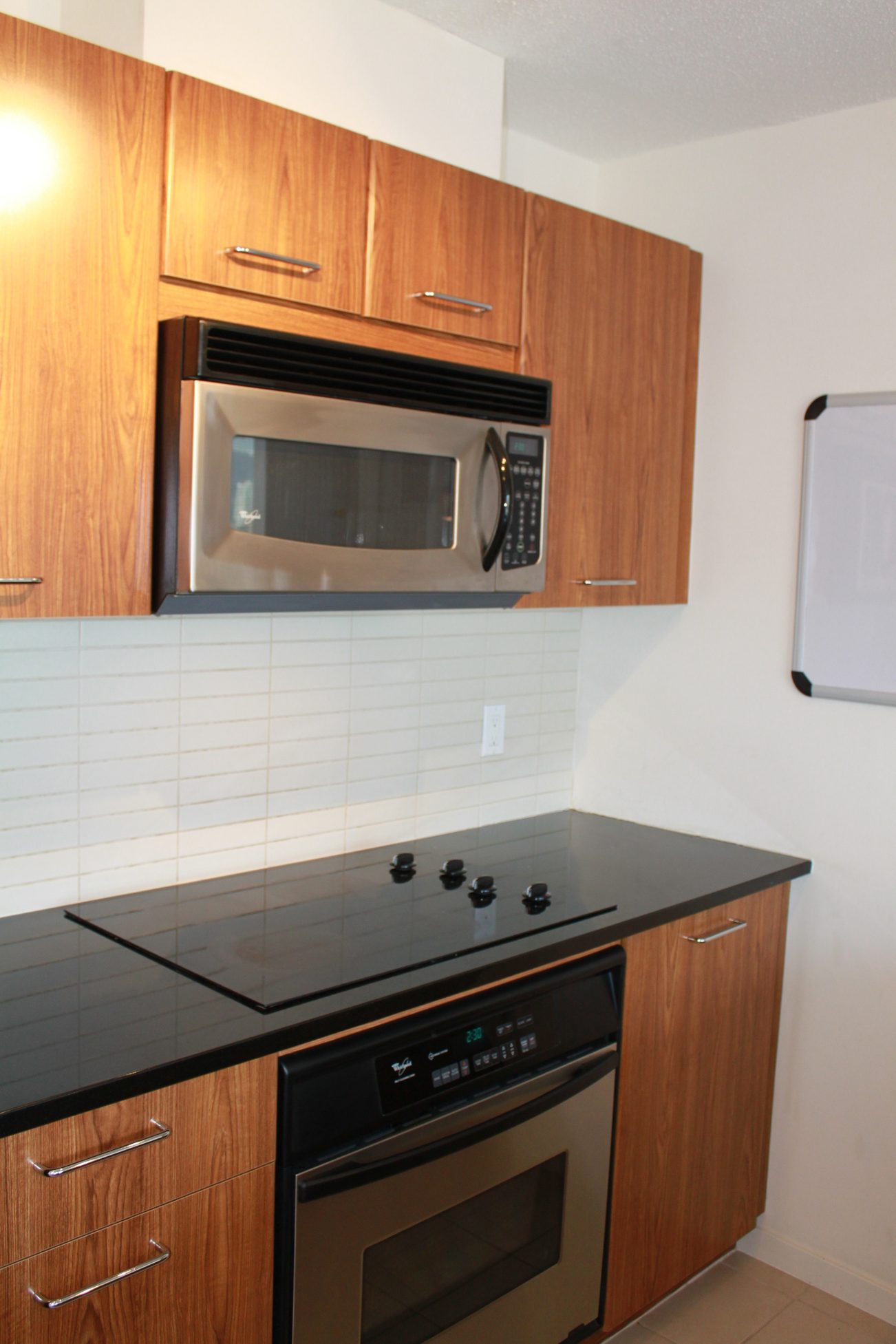 Bright kitchen with black countertops, stainless steel appliances, and wood cabinets. - 2001 - 1199 Seymour, Vancouver Downtown