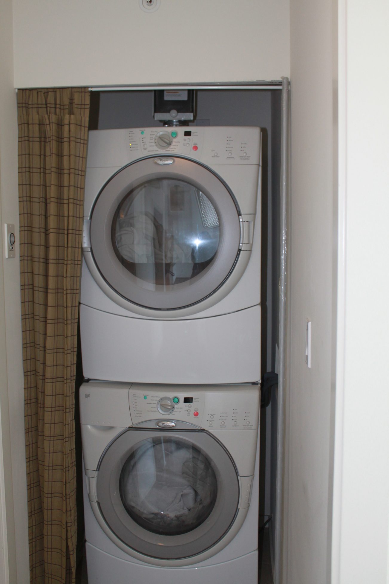 Stacked washer and dryer in a compact laundry area with a curtain. - 2001 - 1199 Seymour, Vancouver Downtown