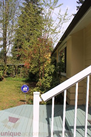 Furnished porch with green deck and white railing, surrounded by lush greenery. - 2156 Cortell Ave, North Vancouver