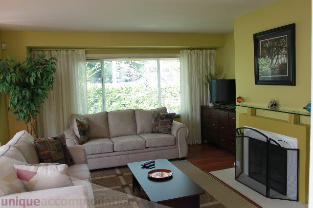 Furnished living room with beige sofas, large window, and green wall art. - 2156 Cortell Ave, North Vancouver