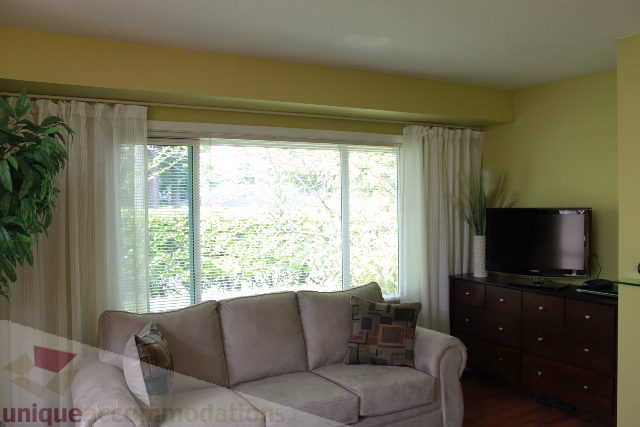 Bright living room with beige furniture, large window, and green plants. - 2156 Cortell Ave, North Vancouver