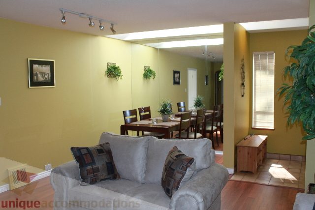 Furnished living room with yellow walls, wooden dining table, and large windows. - 2156 Cortell Ave, North Vancouver