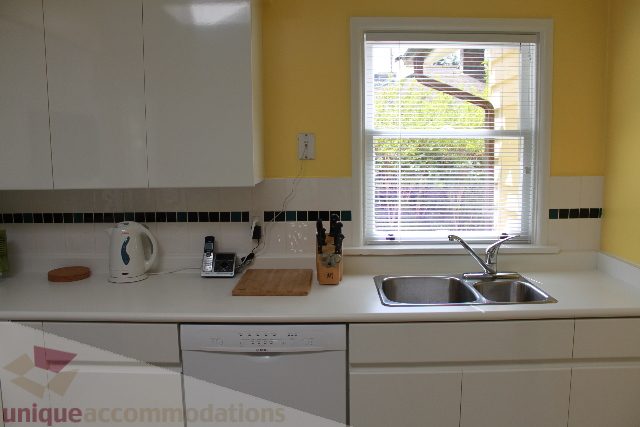Bright kitchen with white cabinets, black tile backsplash, and a window with blinds. - 2156 Cortell Ave, North Vancouver