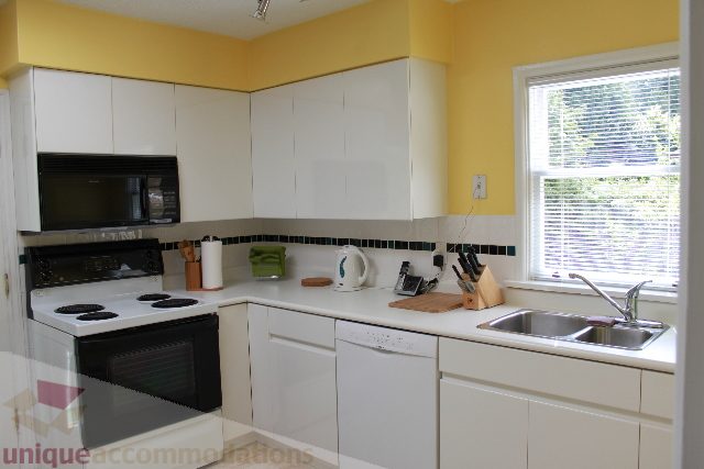 Bright kitchen with white cabinets, black countertops, and a window with blinds. - 2156 Cortell Ave, North Vancouver