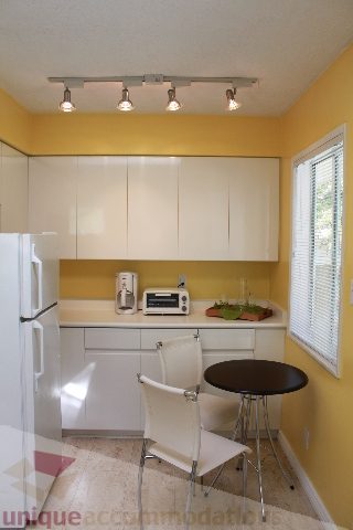 Bright kitchen with white cabinets, yellow backsplash, and a small dining area with white chairs and a black table.