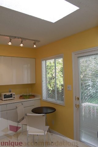 Bright kitchen with yellow walls, white cabinets, and a small round table. - 2156 Cortell Ave, North Vancouver