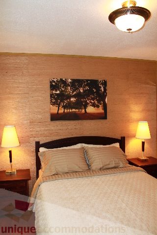 Furnished bedroom with a king-sized bed, nightstands, lamps, and a wall art featuring a tree scene. - 2156 Cortell Ave, North Vancouver