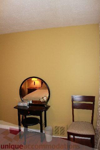 Small bedroom with a vanity mirror and wooden chair, neutral decor. - 2156 Cortell Ave, North Vancouver