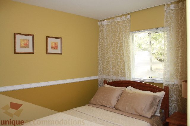 Furnished bedroom with yellow walls, patterned curtains, and framed artwork. - 2156 Cortell Ave, North Vancouver