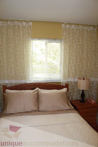Furnished bedroom with patterned curtains and a wooden headboard. - 2156 Cortell Ave, North Vancouver