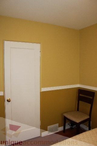 Small bedroom with yellow walls, white door, and wooden chair. - 2156 Cortell Ave, North Vancouver