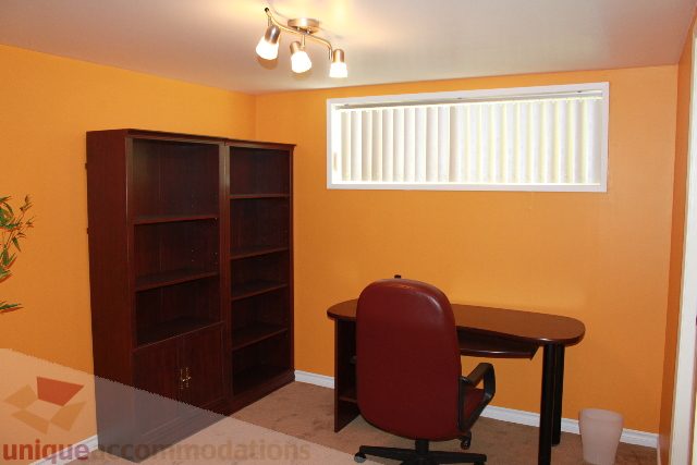 Furnished den with orange walls, bookshelf, and round table. - 2156 Cortell Ave, North Vancouver