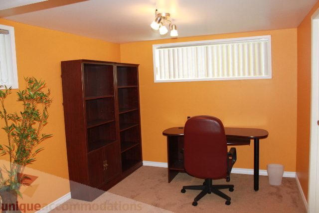 Bright den with orange walls, wooden bookshelf, and desk setup. - 2156 Cortell Ave, North Vancouver
