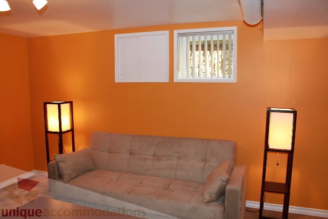 Furnished living room with orange walls, two windows, and a beige sofa. - 2156 Cortell Ave, North Vancouver