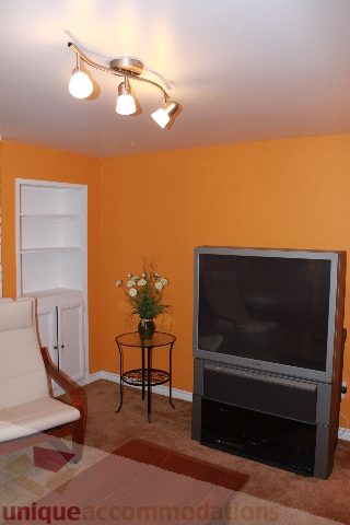 Living room with orange walls, a flat-screen TV, and a small round table with flowers. - 2156 Cortell Ave, North Vancouver