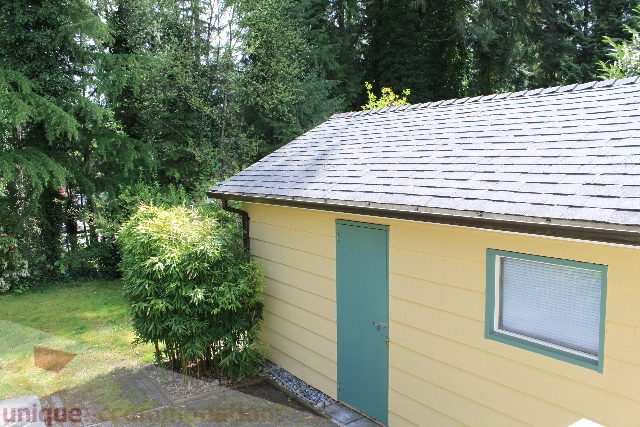 Furnished 2-bedroom + den house with a yellow exterior and gray shingled roof, surrounded by greenery. - 2156 Cortell Ave, North Vancouver