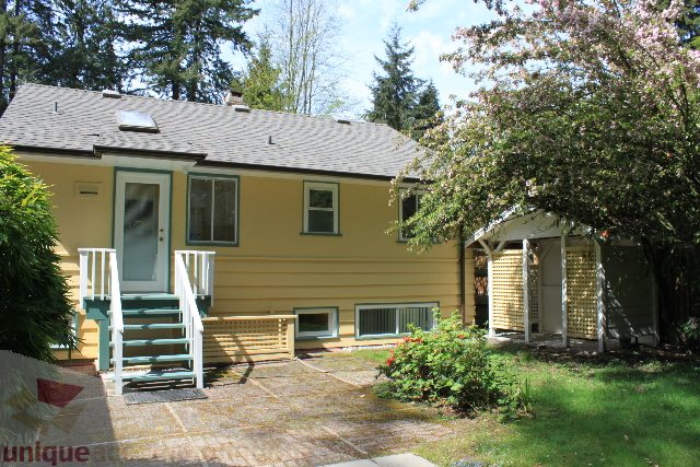 Bright yellow house with a porch and a small garden, surrounded by trees. - 2156 Cortell Ave, North Vancouver
