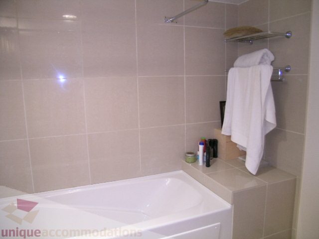 Bathroom with white bathtub, beige tiles, and neatly hung towels. - 2507 - 950 Cambie Street, Vancouver Downtown