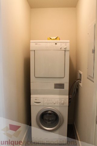Compact laundry room with stacked washer and dryer, white cabinets, and a small countertop. - 2205 - 1077 West Cordova, Vancouver Downtown