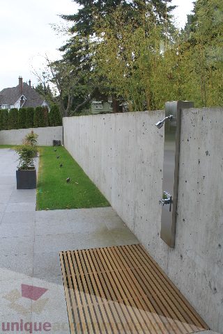 Fenced backyard with modern concrete wall and water feature, grassy area, and trees in the background. - 6012 Newton Wynd, Vancouver West Side