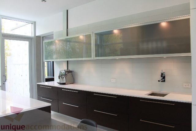 Bright kitchen with modern white cabinets, stainless steel backsplash, and large windows. - 6012 Newton Wynd, Vancouver West Side