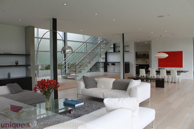 Modern living room with white furniture, hardwood floors, and a red abstract painting. - 6012 Newton Wynd, Vancouver West Side