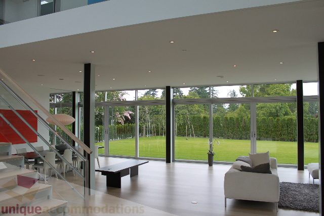 Spacious living room with large windows, modern furnishings, and a view of greenery. - 6012 Newton Wynd, Vancouver West Side