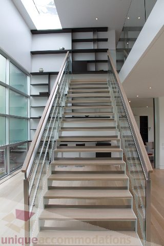 Modern staircase with glass railings and wooden steps leading to upper floor. - 6012 Newton Wynd, Vancouver West Side