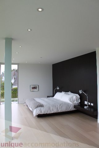 Spacious bedroom with modern black accent wall, hardwood floors, and city view. - 6012 Newton Wynd, Vancouver West Side