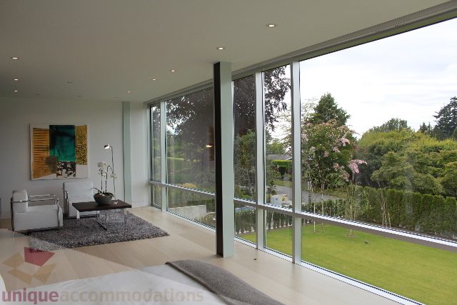 Bright living room with large windows, modern decor, and a view of greenery. - 6012 Newton Wynd, Vancouver West Side