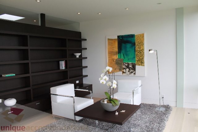 Bright living room with modern decor, dark shelving, and abstract wall art. - 6012 Newton Wynd, Vancouver West Side