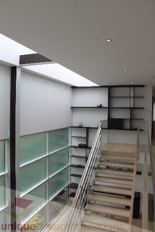 Modern open-concept living area with glass shelves and wooden staircase. - 6012 Newton Wynd, Vancouver West Side