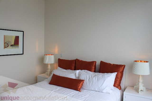 Bright bedroom with white bedding and orange pillows, modern lamp, abstract wall art. - 6002 - 1128 West Georgia, Vancouver Downtown