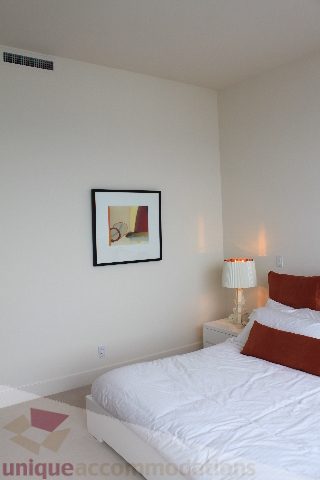 Bright bedroom with white bedding, orange pillows, and framed artwork on the wall. - 6002 - 1128 West Georgia, Vancouver Downtown