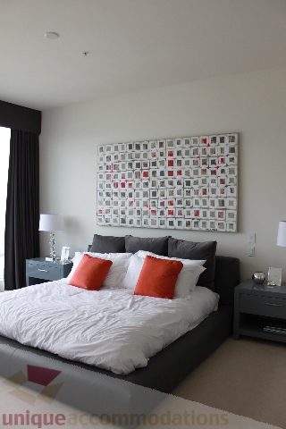 Spacious bedroom with modern decor, large bed, orange pillows, and abstract wall art. - 6002 - 1128 West Georgia, Vancouver Downtown