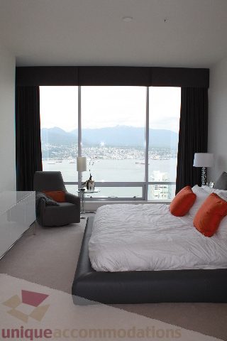 Bright bedroom with large windows offering a stunning city view, modern furnishings, and a cozy ambiance.