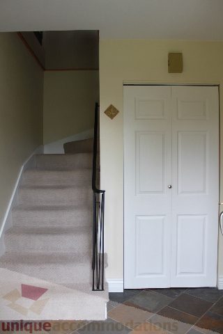 Entryway with carpeted stairs leading up and a white door with a gold handle. - 2730 Ailsa Crescent, North Vancouver
