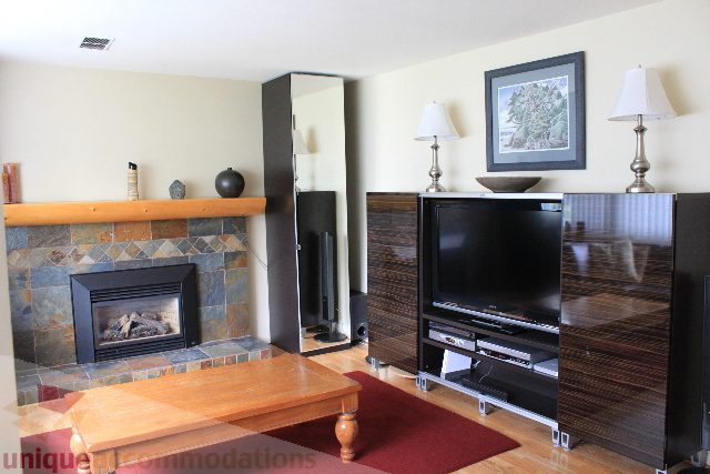 Living room with stone fireplace, hardwood floors, and a modern TV setup. - 2730 Ailsa Crescent, North Vancouver